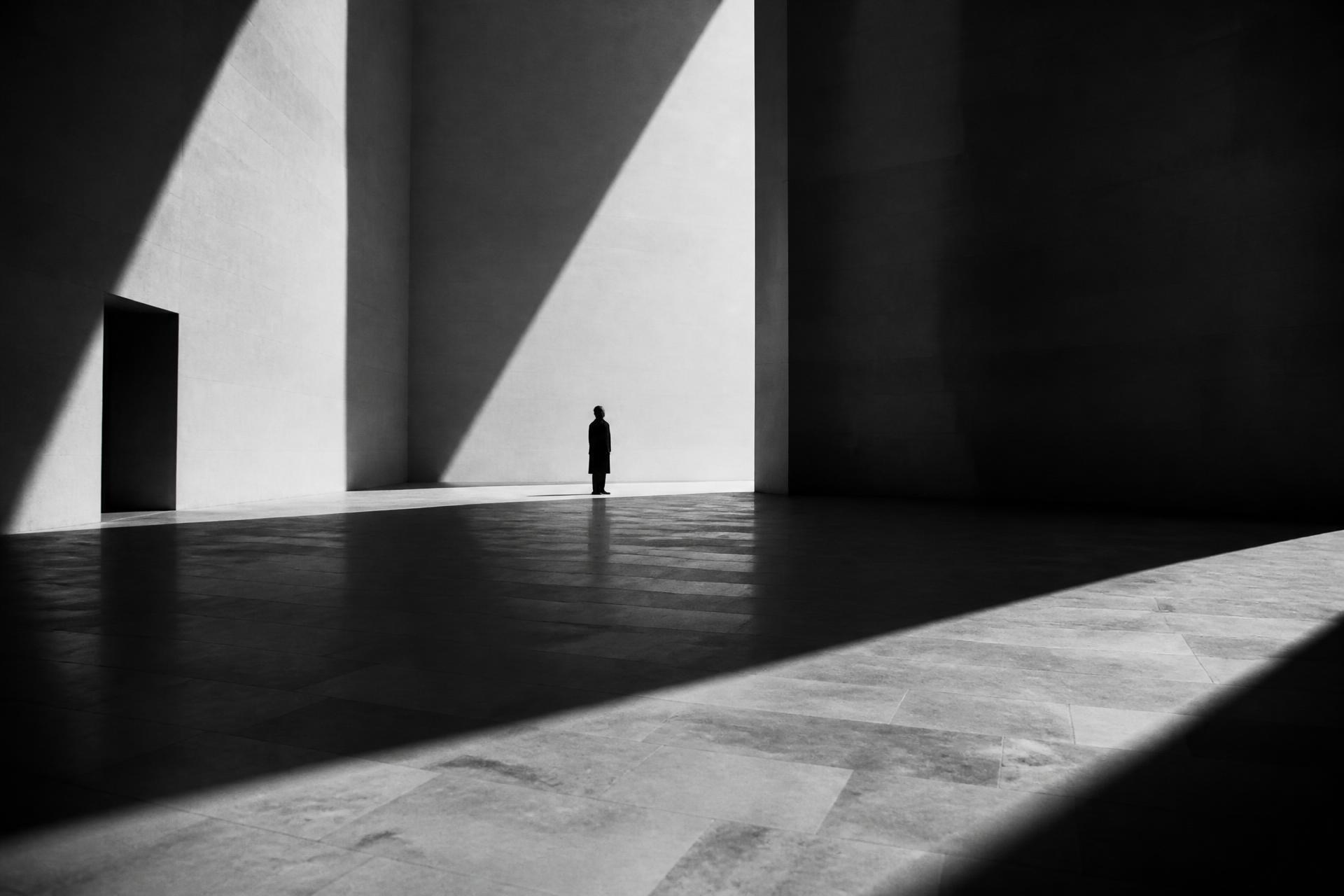 Lone figure in a vast sunlit concrete hall, fine art black and white photograph